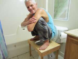 Brett demonstrating full squat on squatting toilet platform for natural elimination.